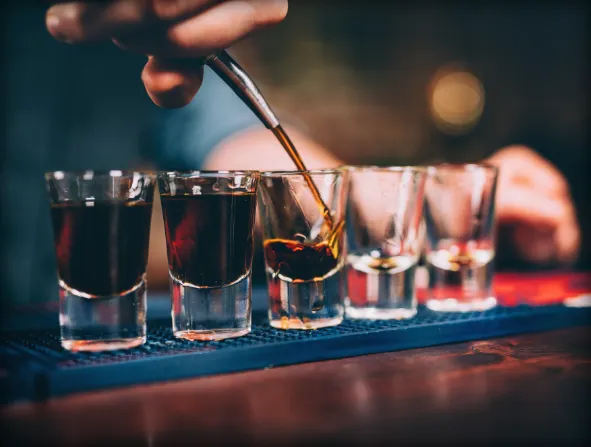Hand preparing shots with a dark liquid on a bar mat.